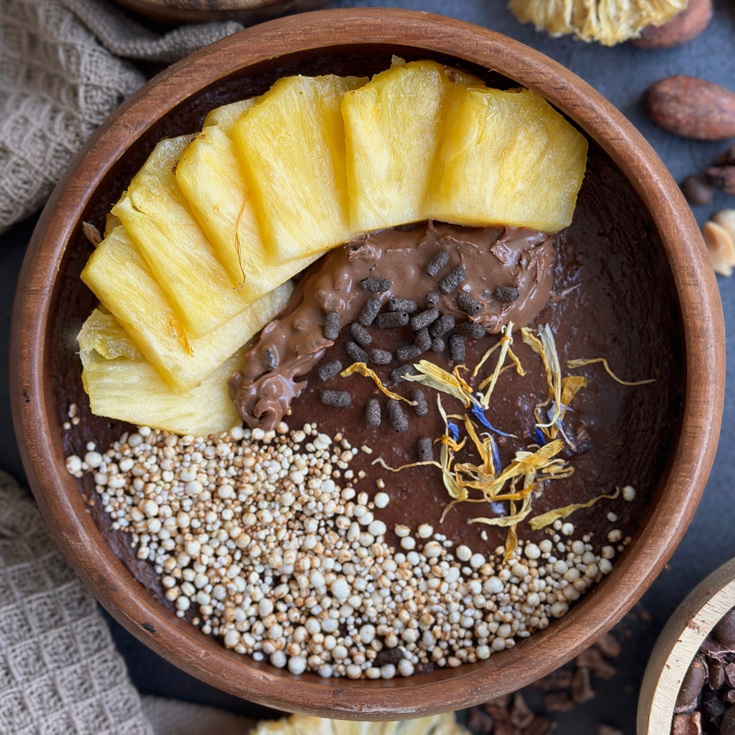 Cremige Ananas Schoko Haferbowl mit frischen Ananasstücken, dunklem Schoko-Protein-Spread und knackigem Topping in einer Schale angerichtet.
