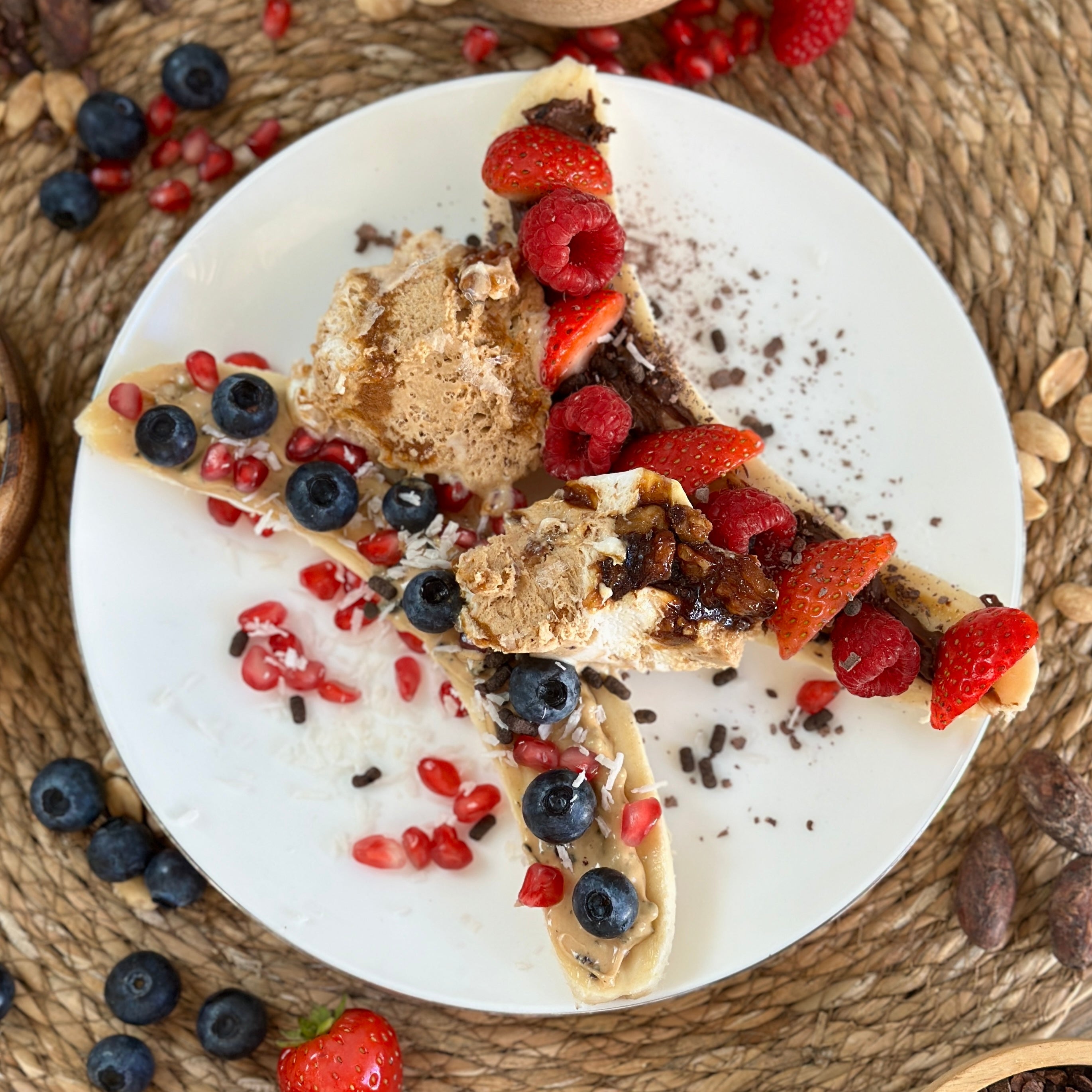 High Protein Banana Split auf einem Teller: längs halbierte Banane mit cremigem Protein Spread, frischen Beeren und dunklen Schokoladensplittern als Topping.