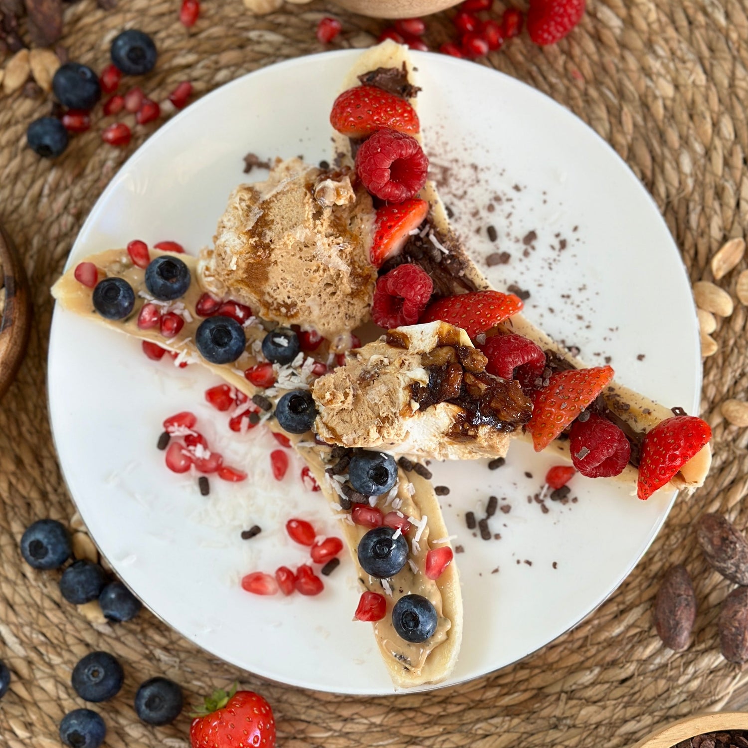 High Protein Banana Split auf einem Teller: längs halbierte Banane mit cremigem Protein Spread, frischen Beeren und dunklen Schokoladensplittern als Topping.