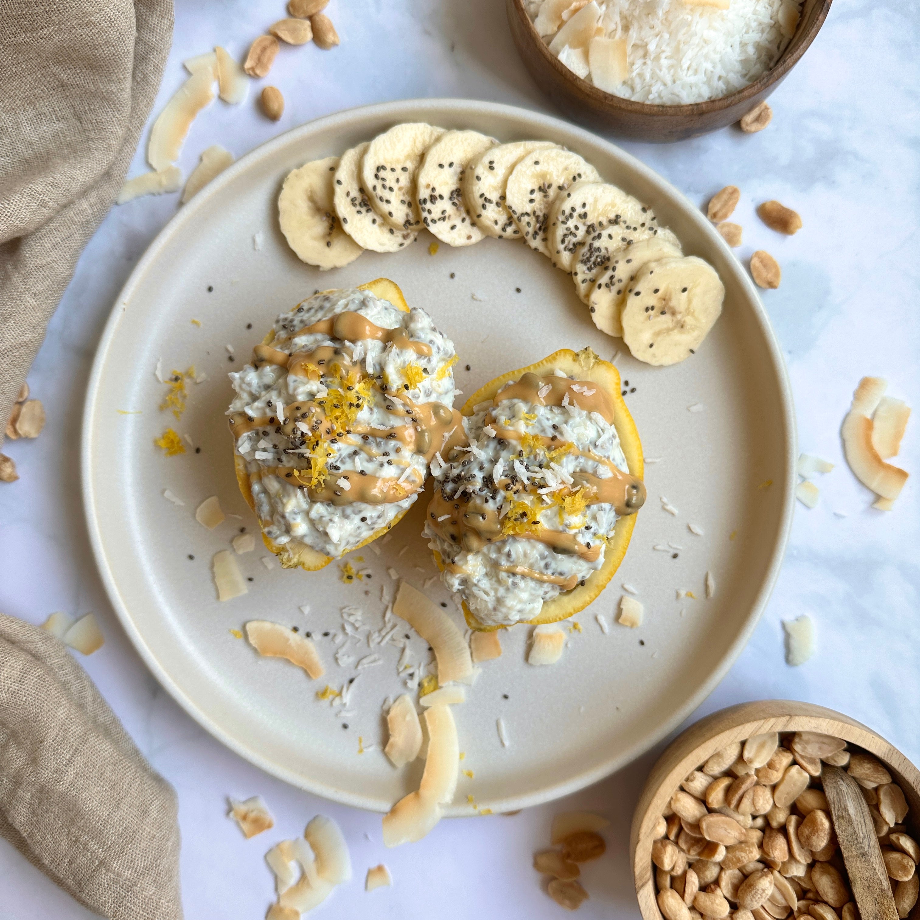 Kokos-Zitronen Chiapudding in ausgehöhlten Zitronenhälften serviert, getoppt mit cremigem Protein-Spread und Kokosraspeln.
