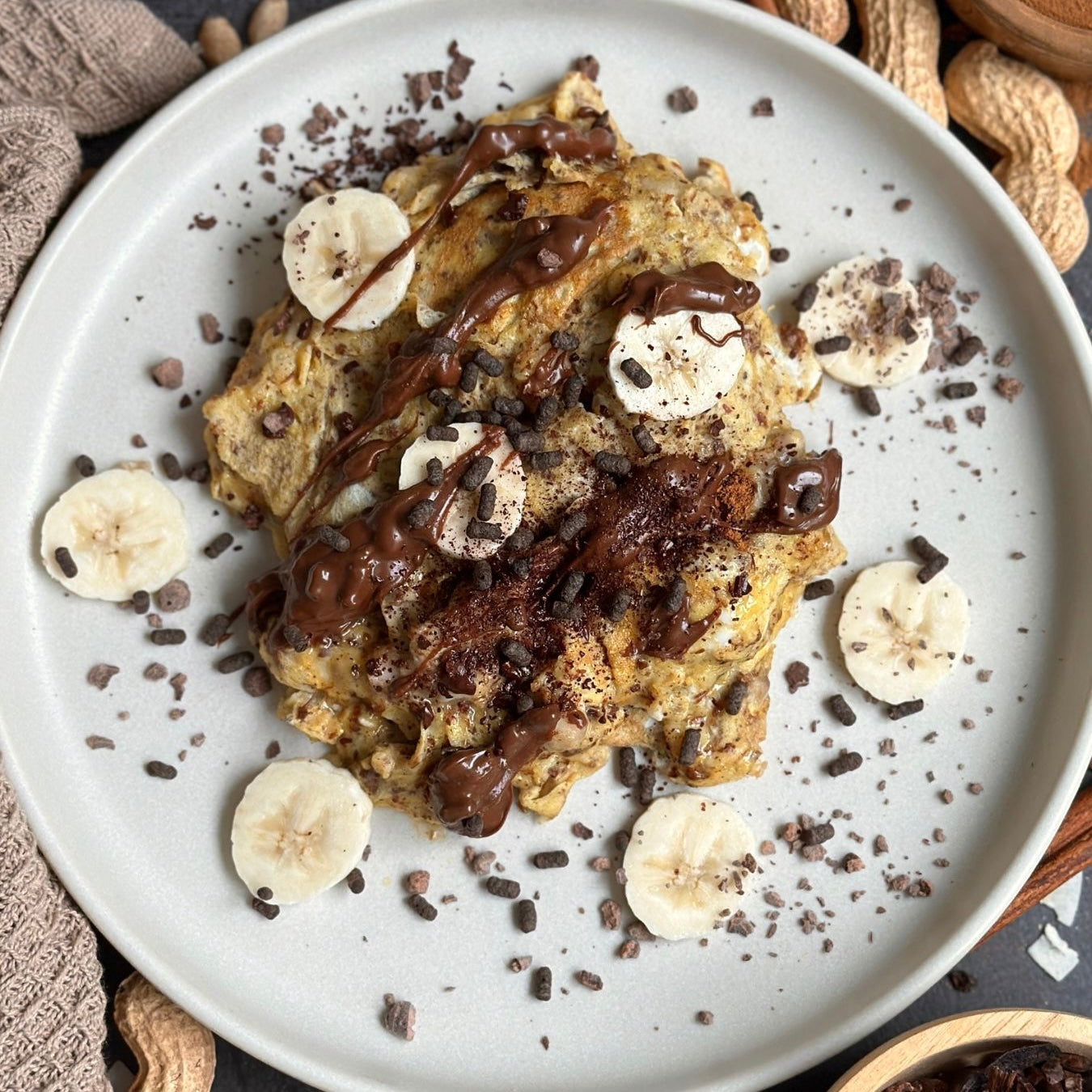 Schoko-Bananen Rührei auf einem Teller angerichtet, mit cremigem Protein Schoko Spread und Kakaonibs garniert.
