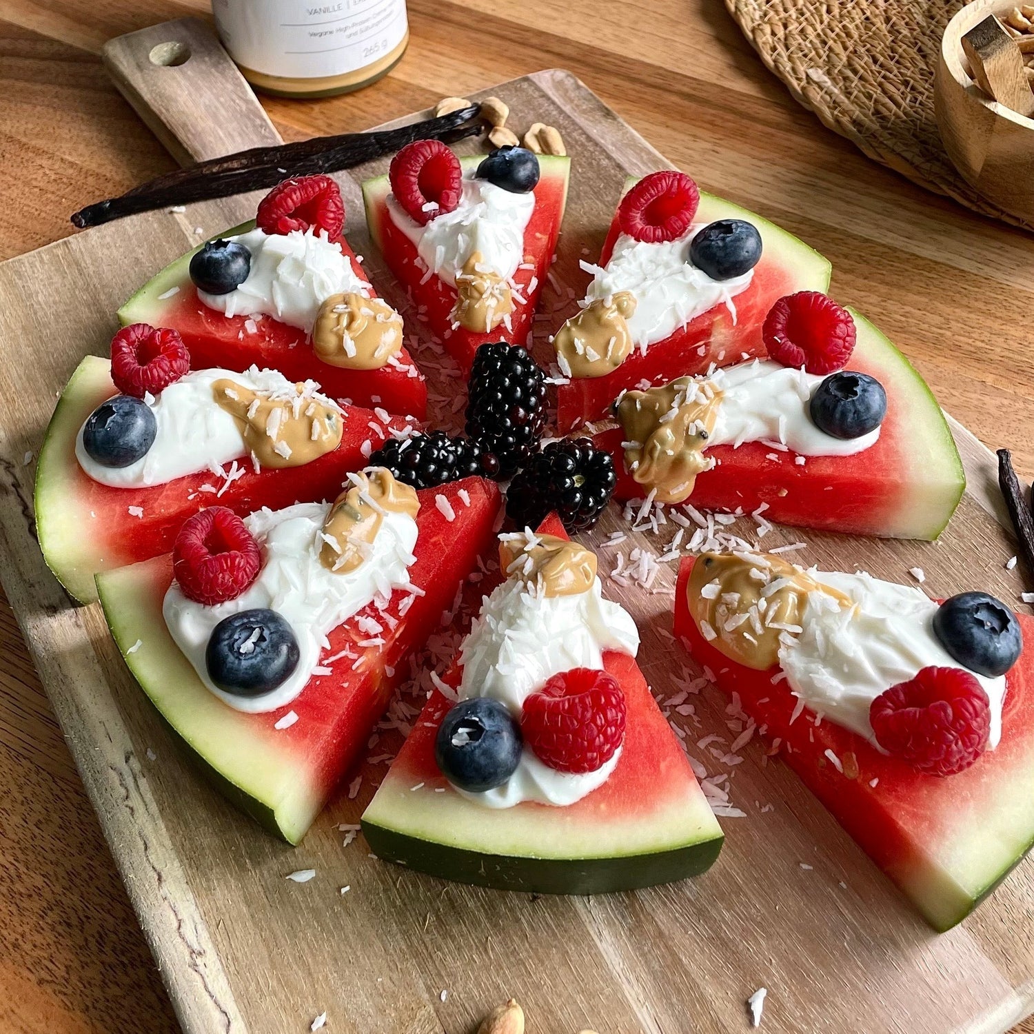 Bunte Wassermelonen-Pizza mit Quark-Protein-Creme und frischen Beeren aufgeschnitten wie Pizzastücke.