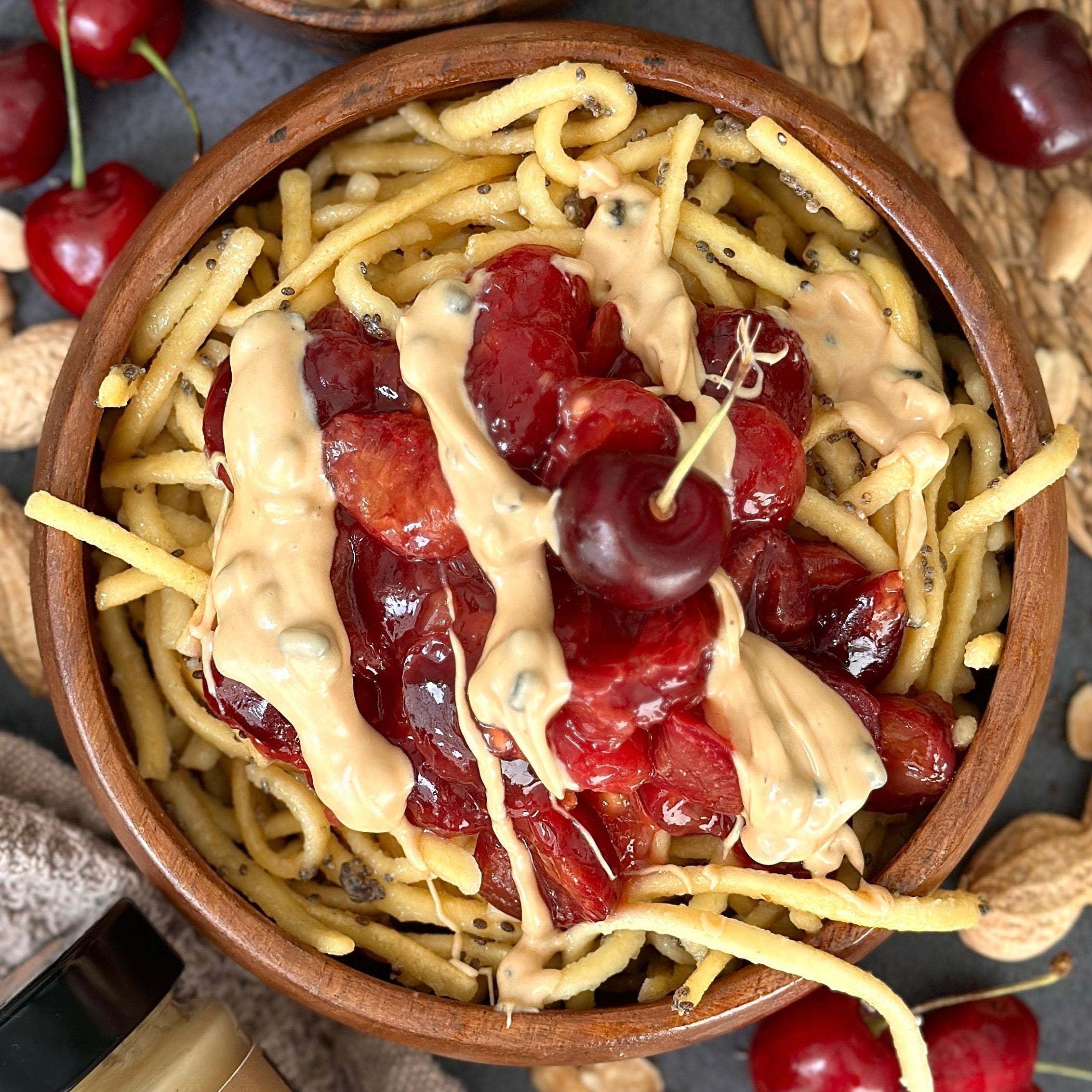 Mohnspätzle mit Kirschkompott in einer Schale serviert, getoppt mit cremigem Erdnuss Protein Spread.